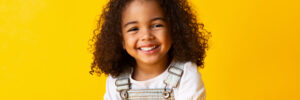 Happy african-american child girl smiling to camera over yellow background